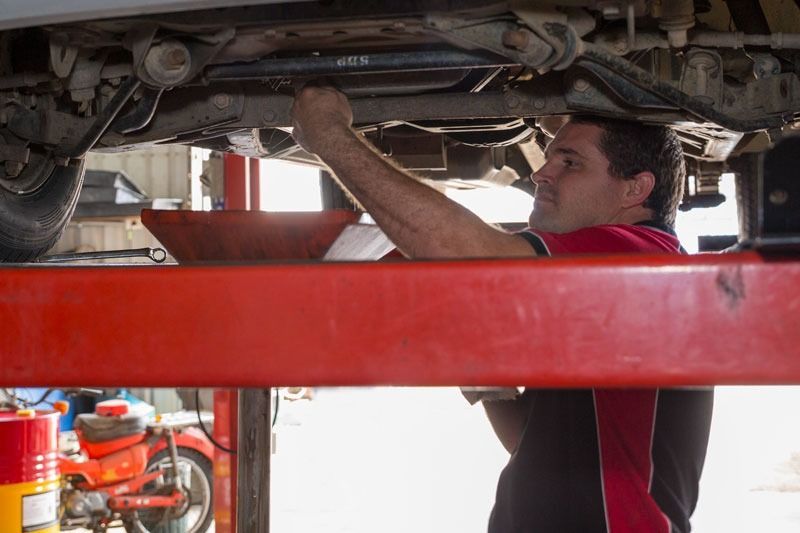 A Man Is Working Under A Car On A Lift In A Garage — CS Mechanical Repairs & Services In Wauchope, NSW