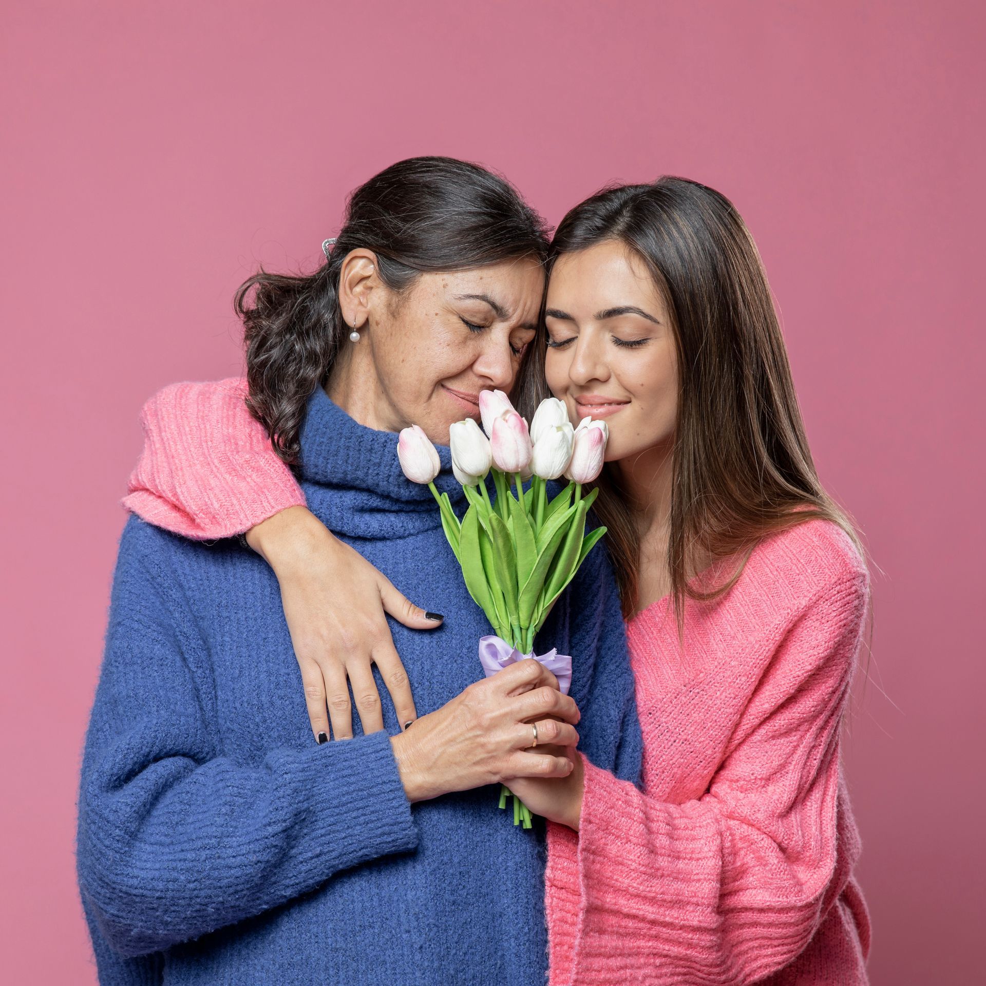 A mother and daughter are hugging and holding a bouquet of flowers.