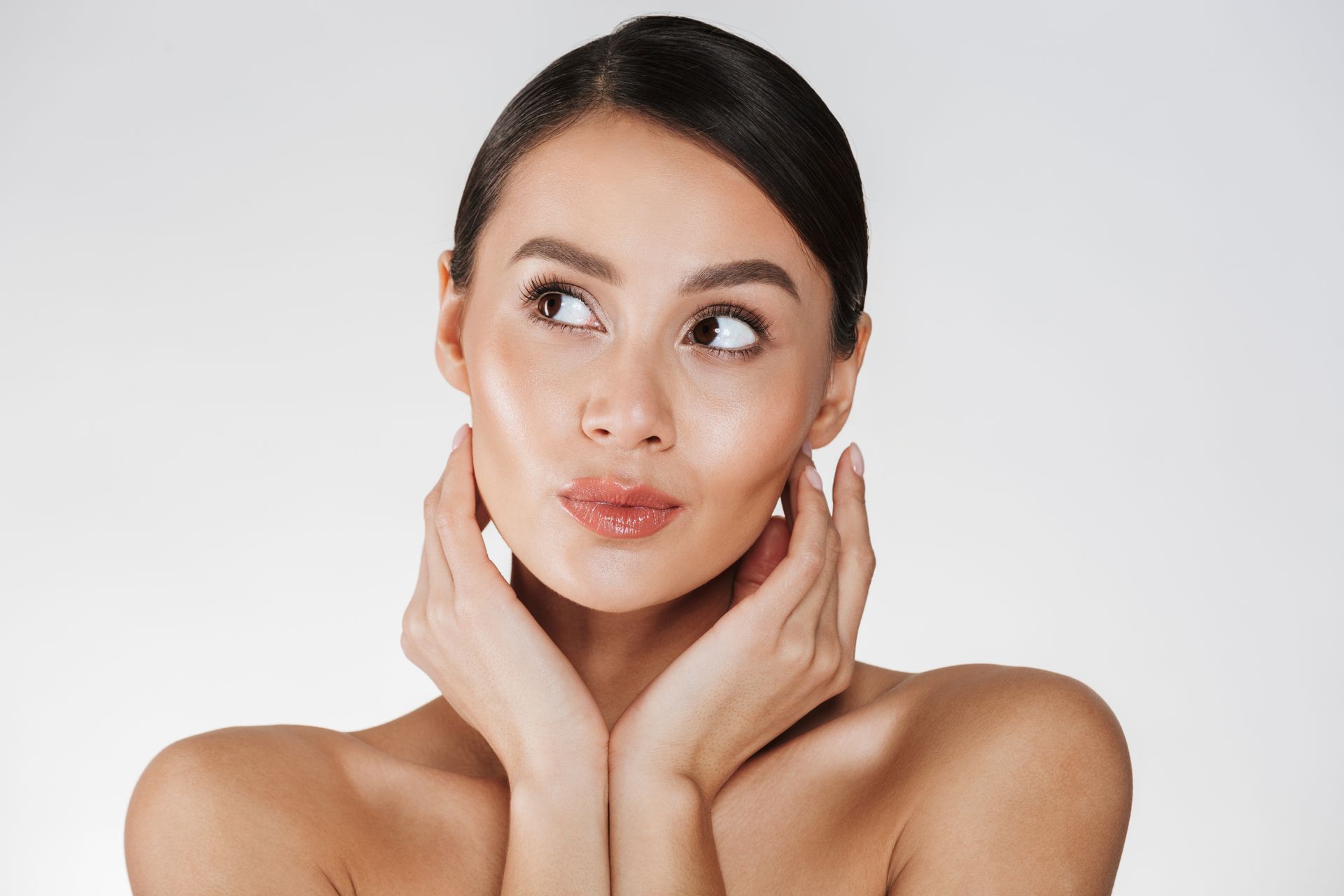 A woman is holding her face with her hands and looking up.