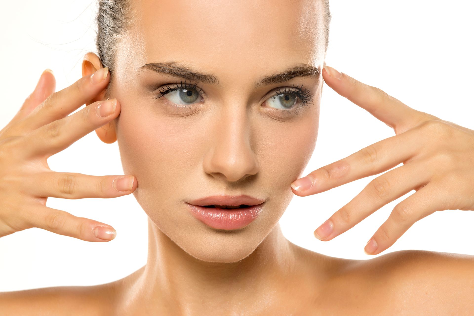 Woman with fair skin touches her face, looking slightly to the side with a neutral expression.