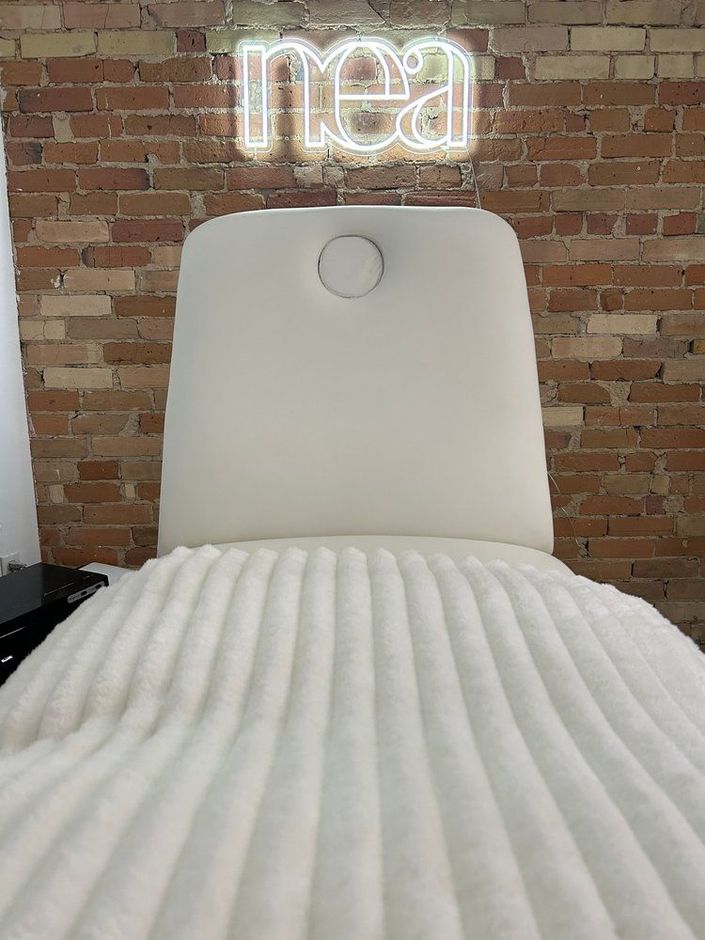 A white chair is sitting in front of a brick wall with a neon sign above it.