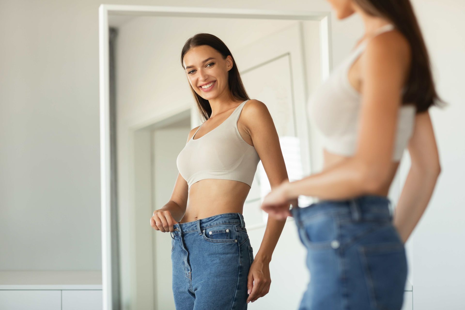 A woman is measuring her waist in front of a mirror.