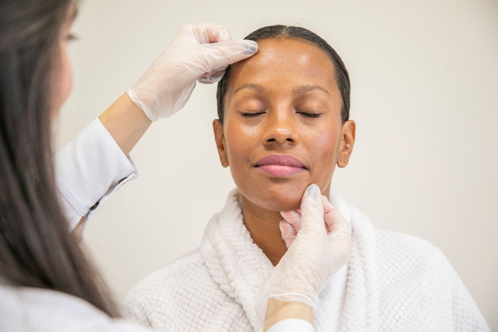Person receiving a facial examination from a professional, wearing gloves, in a white room.
