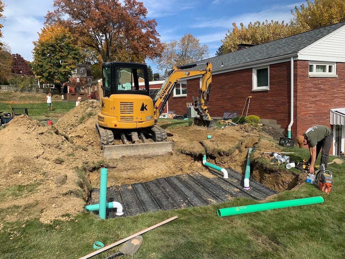 A yellow bulldozer is digging a hole in front of a brick house.