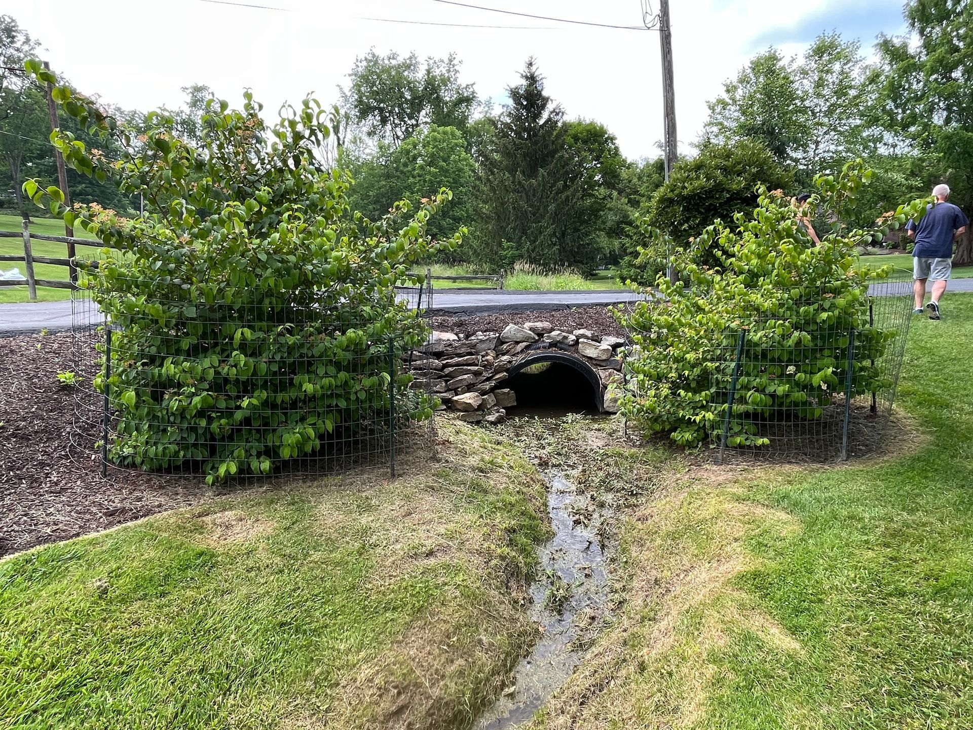 A man is walking across a stone bridge over a muddy stream.