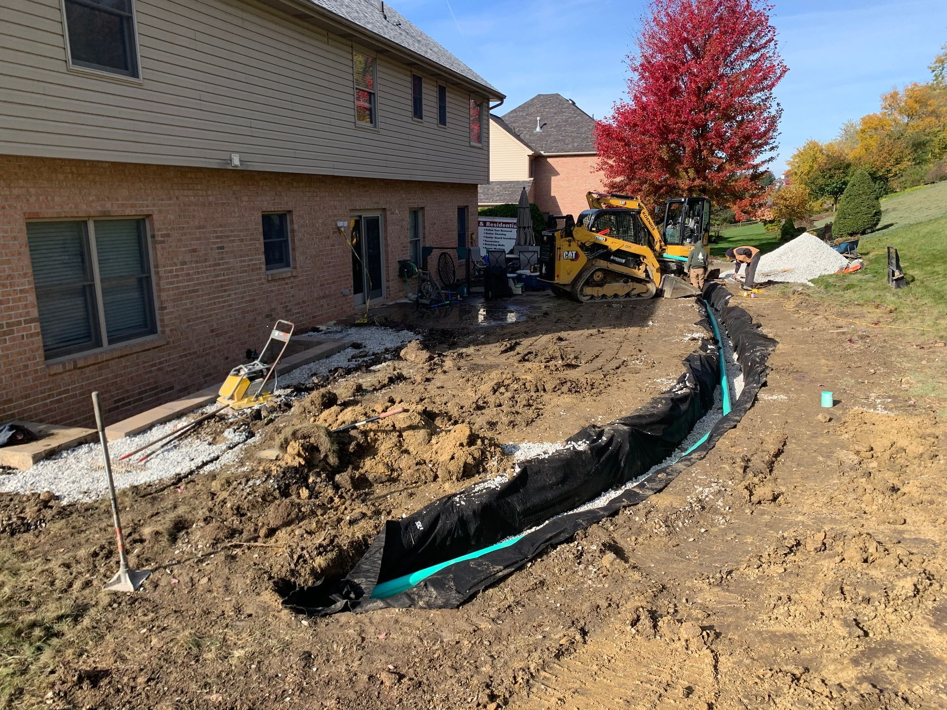 A yellow excavator is digging a hole in the ground in front of a house.