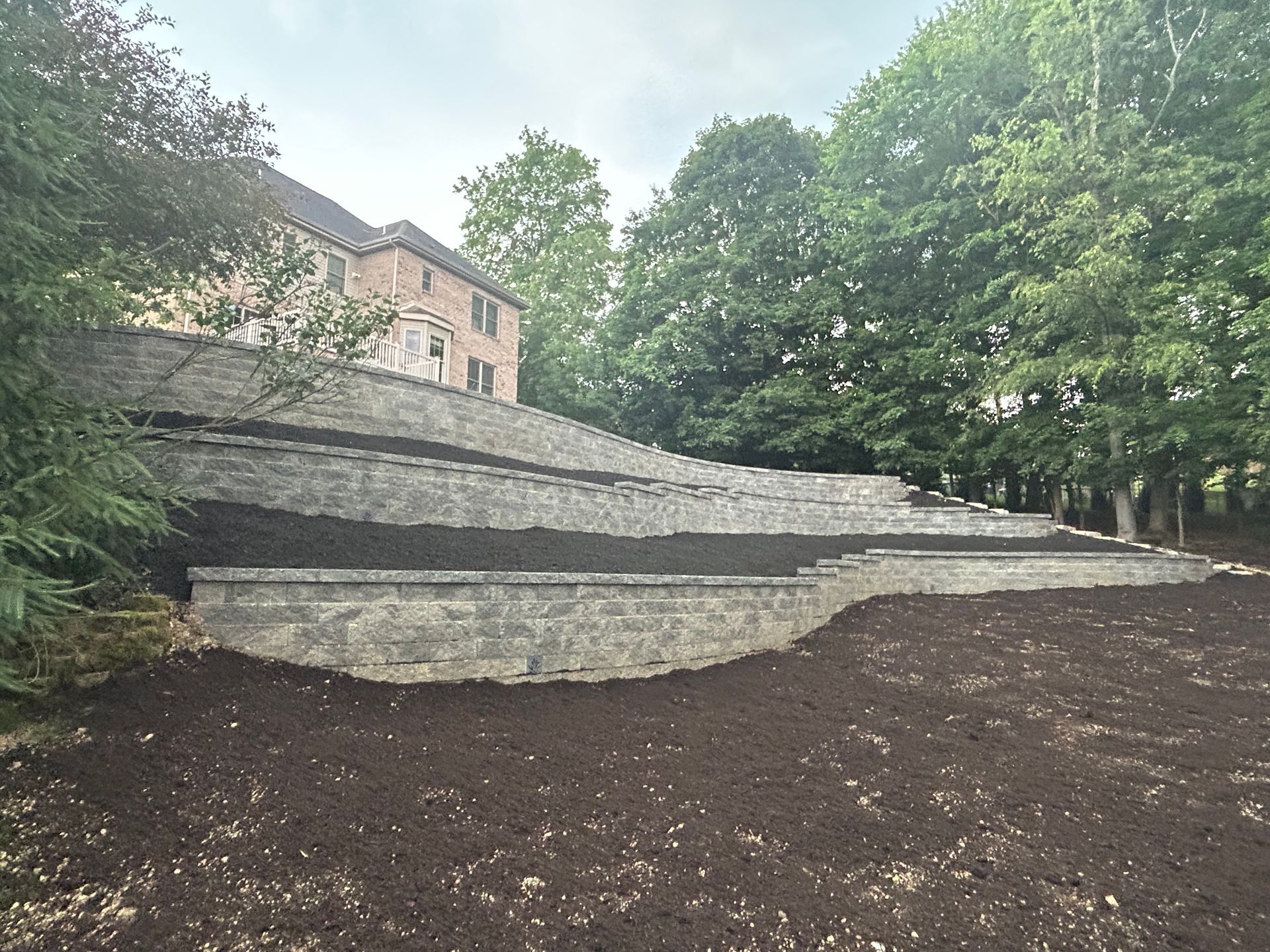 A large stone wall is surrounded by trees and dirt in a park.