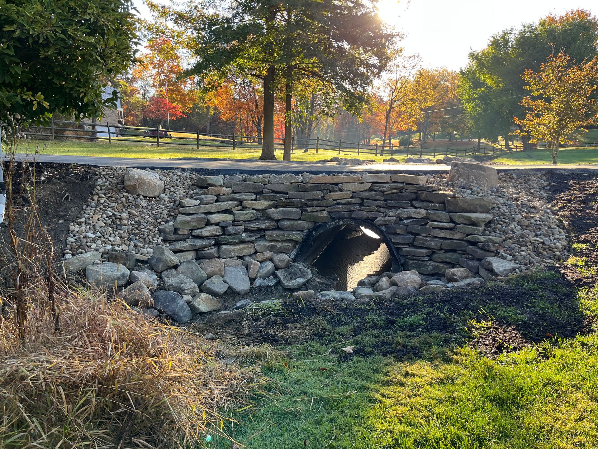 A stone bridge over a stream in a park with trees in the background.