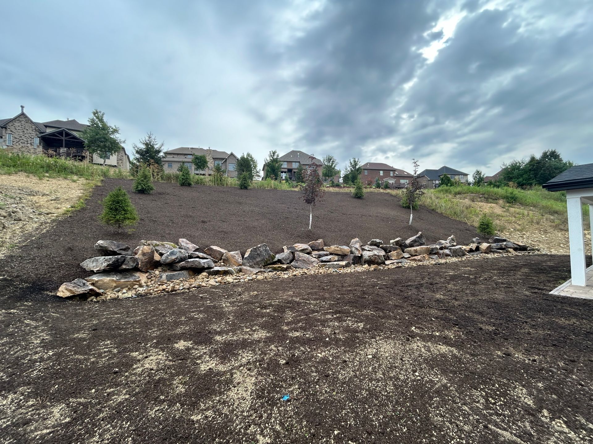 A large pile of dirt and rocks on top of a hill with houses in the background.