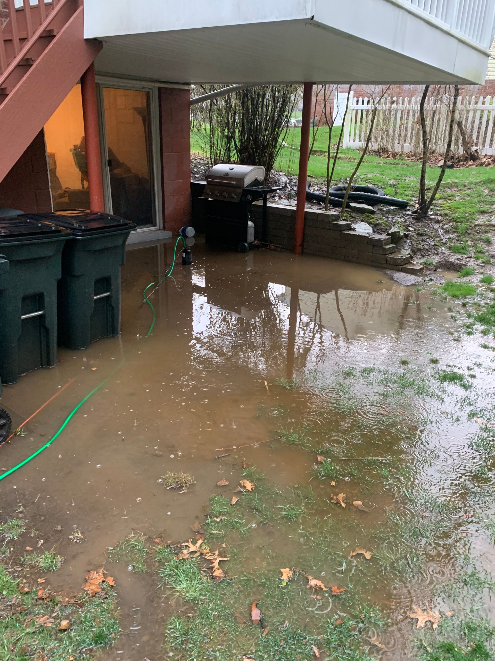 A flooded backyard with trash cans and a hose.