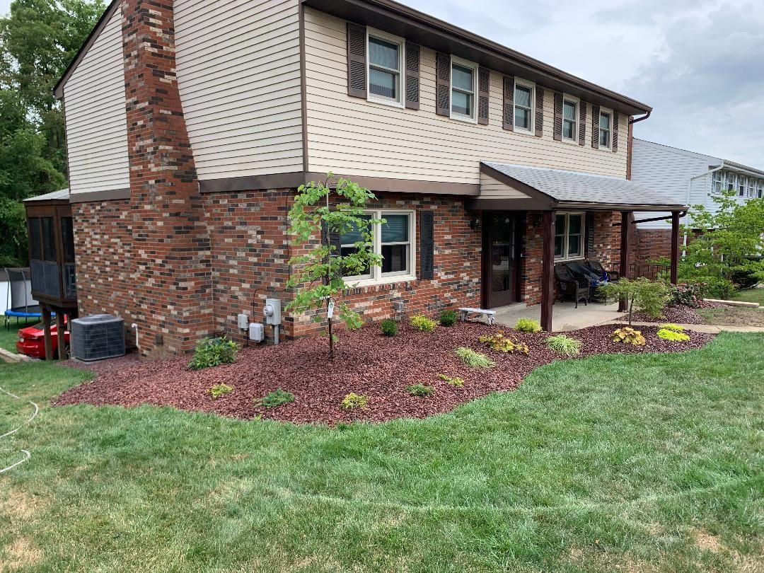 A brick house with a porch and a lush green lawn in front of it.