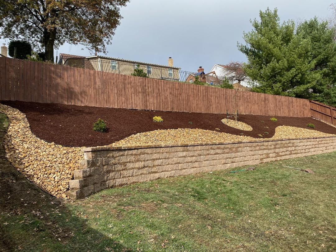 A brick wall surrounded by mulch and a wooden fence.
