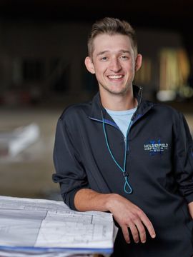 A young man is standing next to a pile of blueprints and smiling.