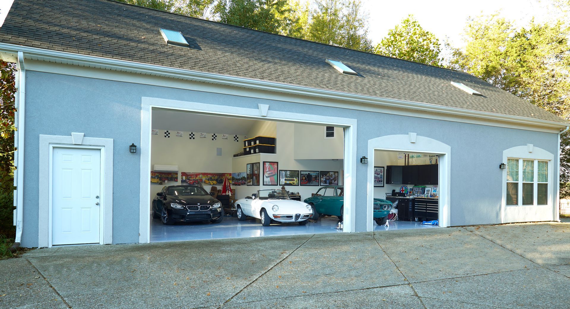 Three cars are parked in a garage with the doors open
