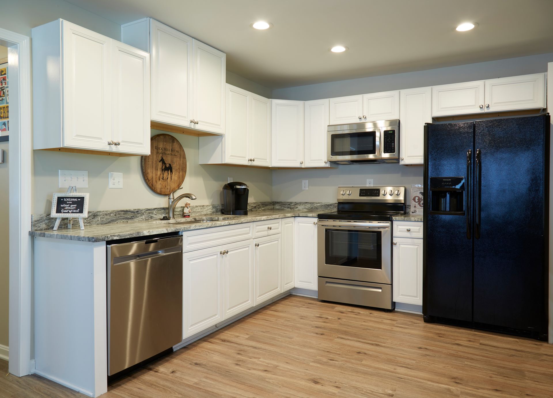 A kitchen with white cabinets , stainless steel appliances , and a black refrigerator.