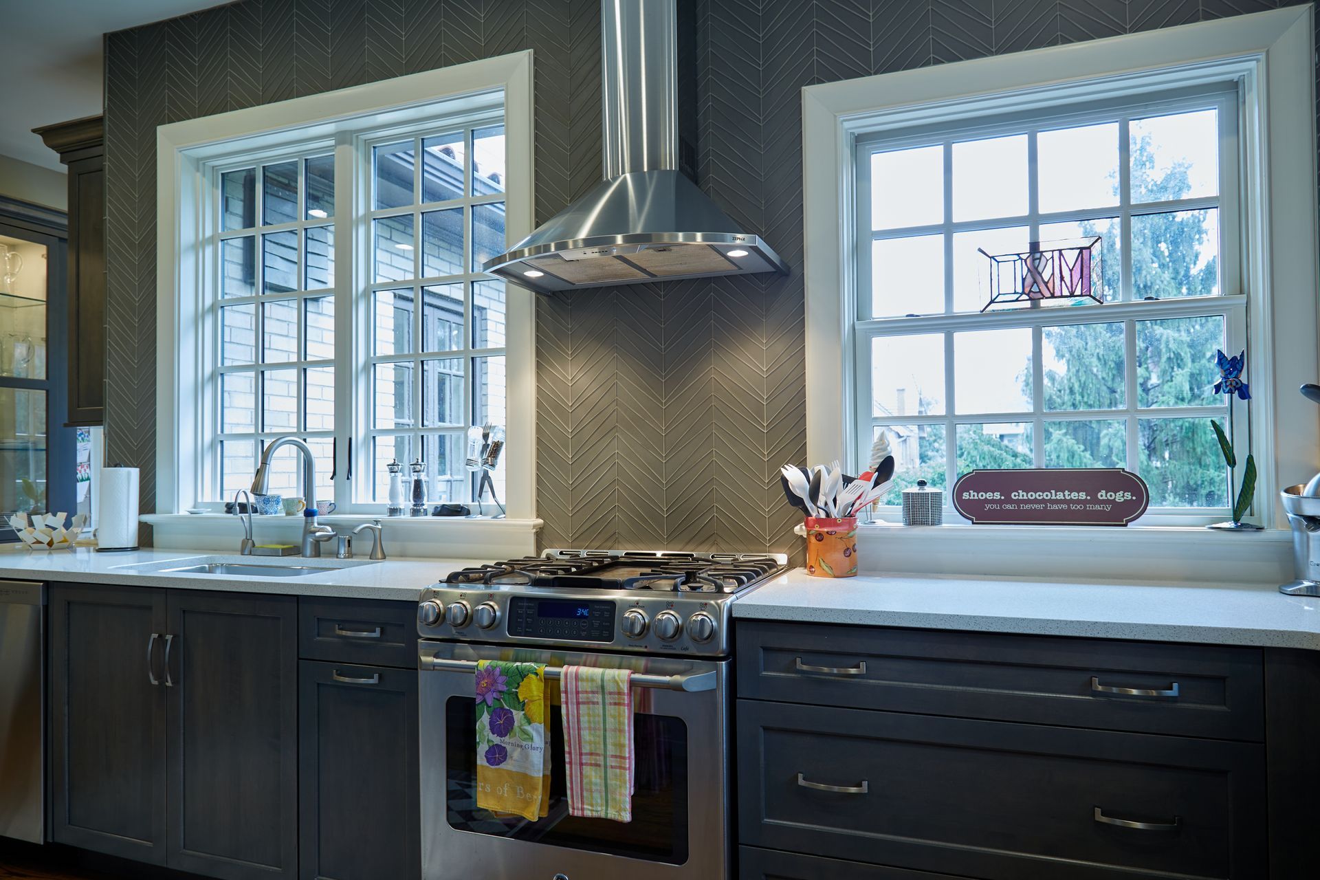 A kitchen with a stove , sink , and two windows