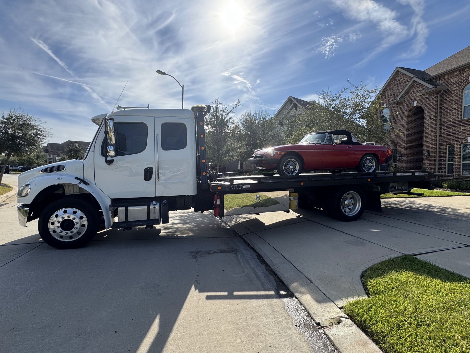White Porsche sports car on a white tow truck bed in front of a building.
