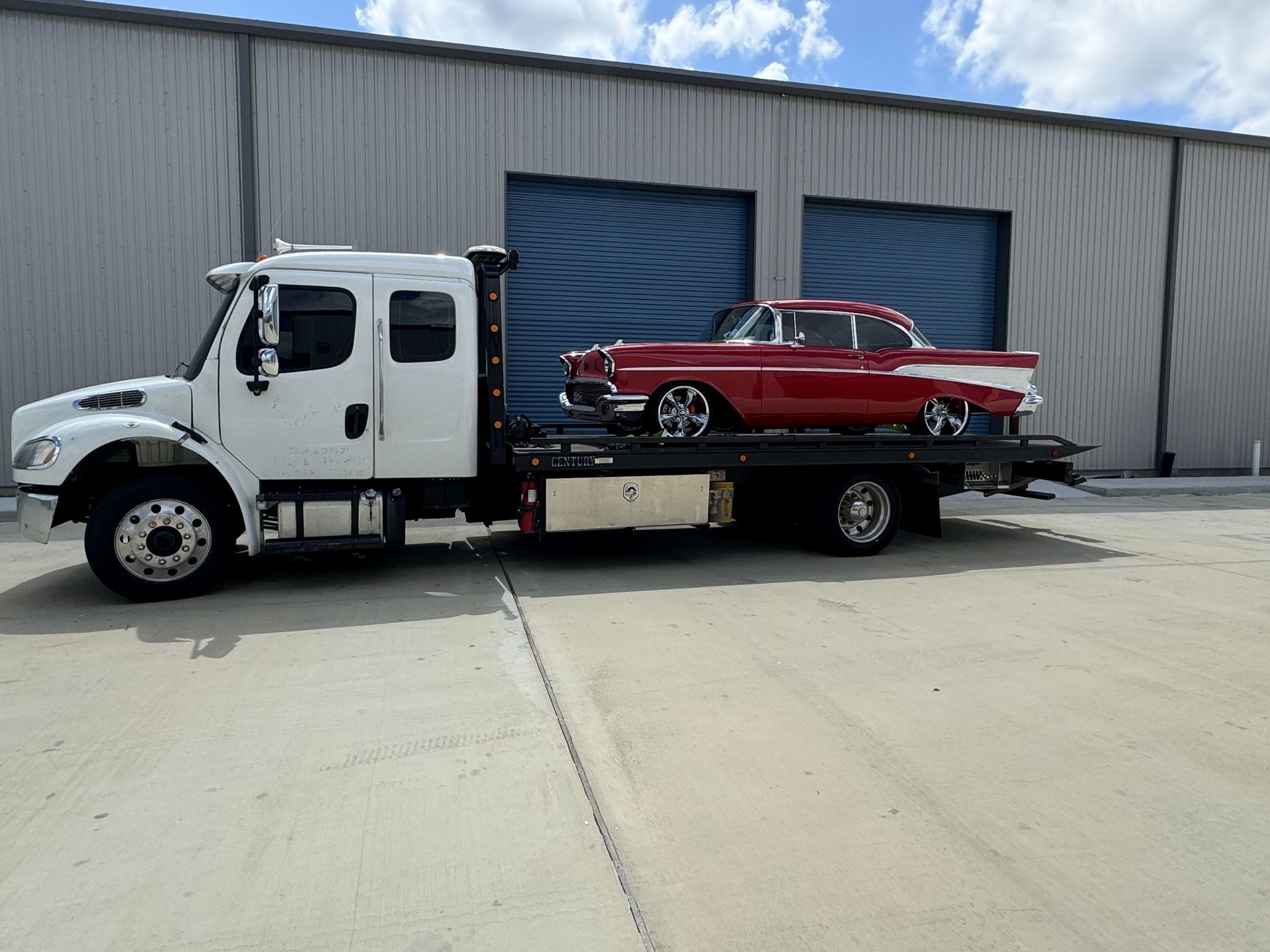 White tow truck carrying a red classic car parked outside a building.