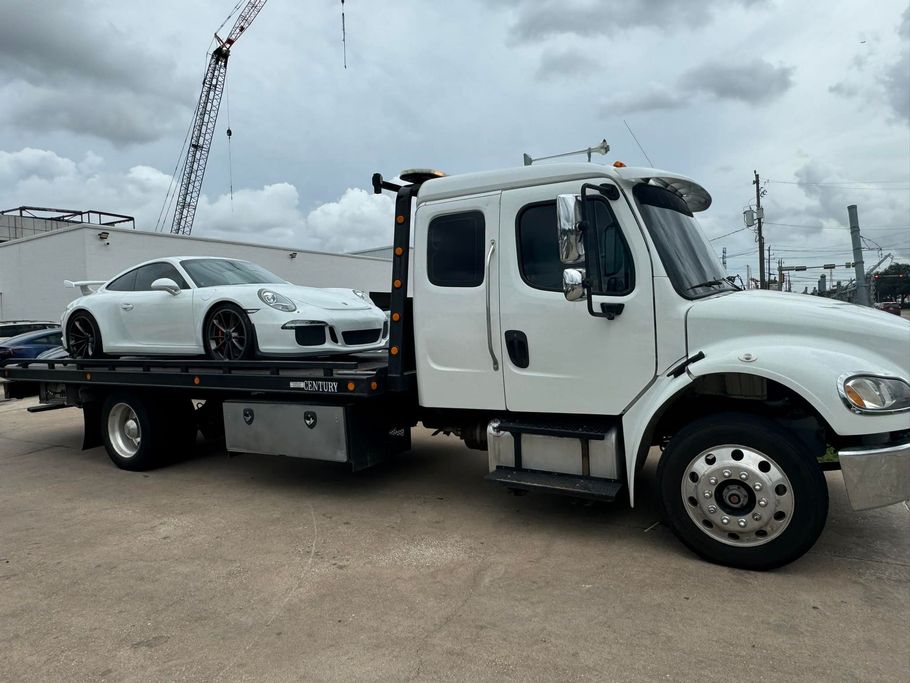 White Porsche sports car loaded on a white tow truck on a cloudy day.