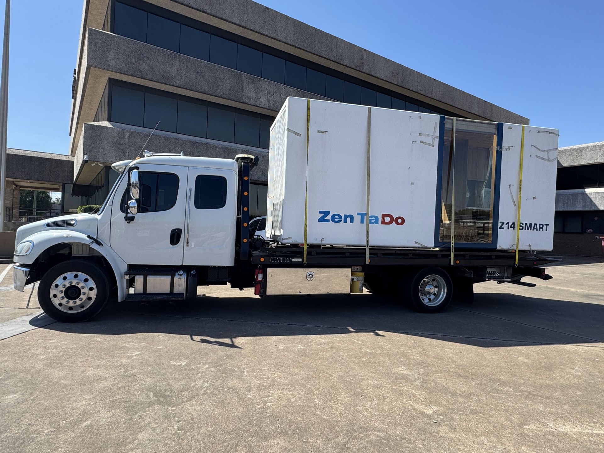 Red classic car on a white tow truck in front of a gray industrial building.