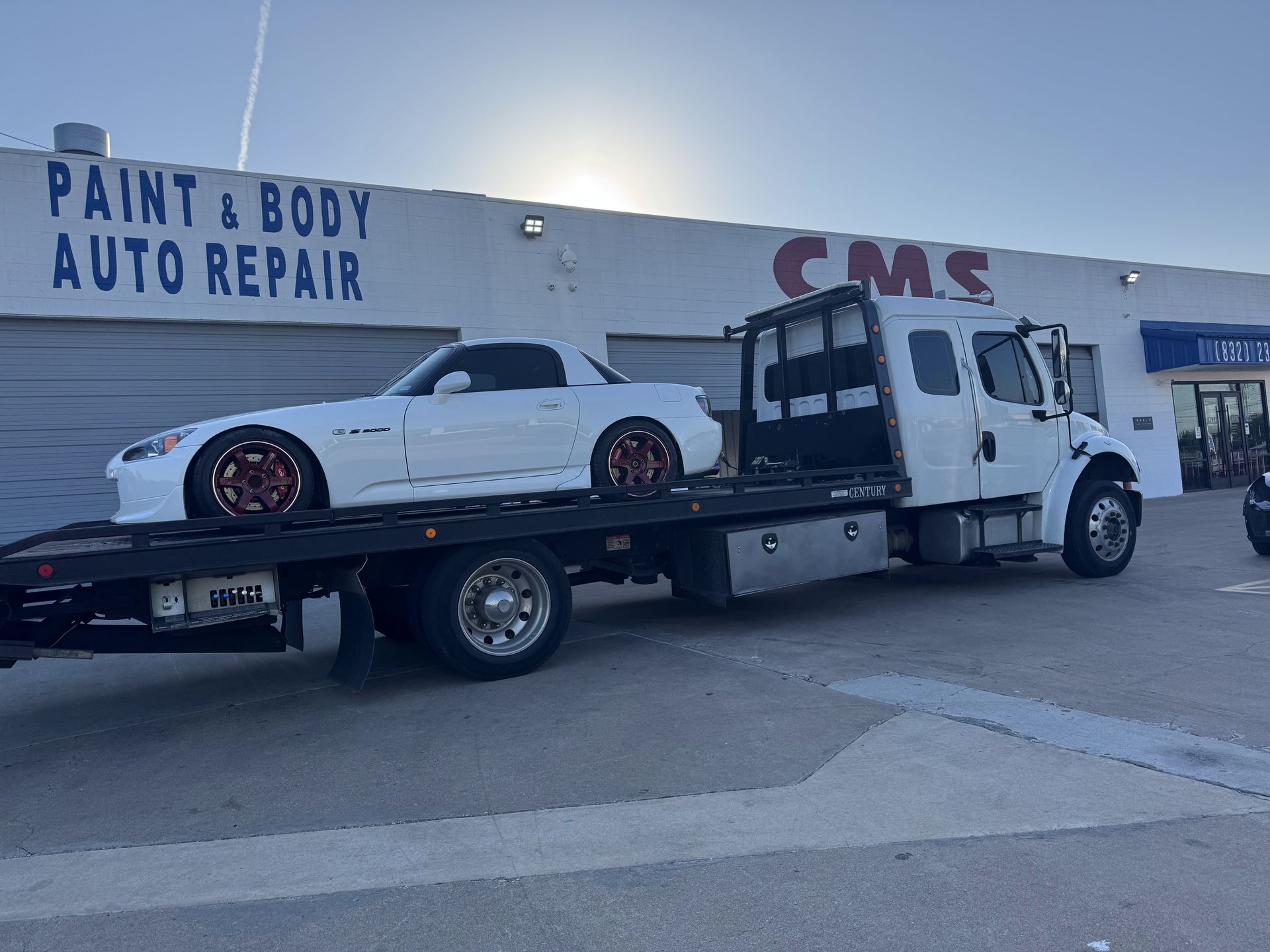 White Porsche sports car on a white tow truck. Outdoors with a crane and cloudy sky in the background.