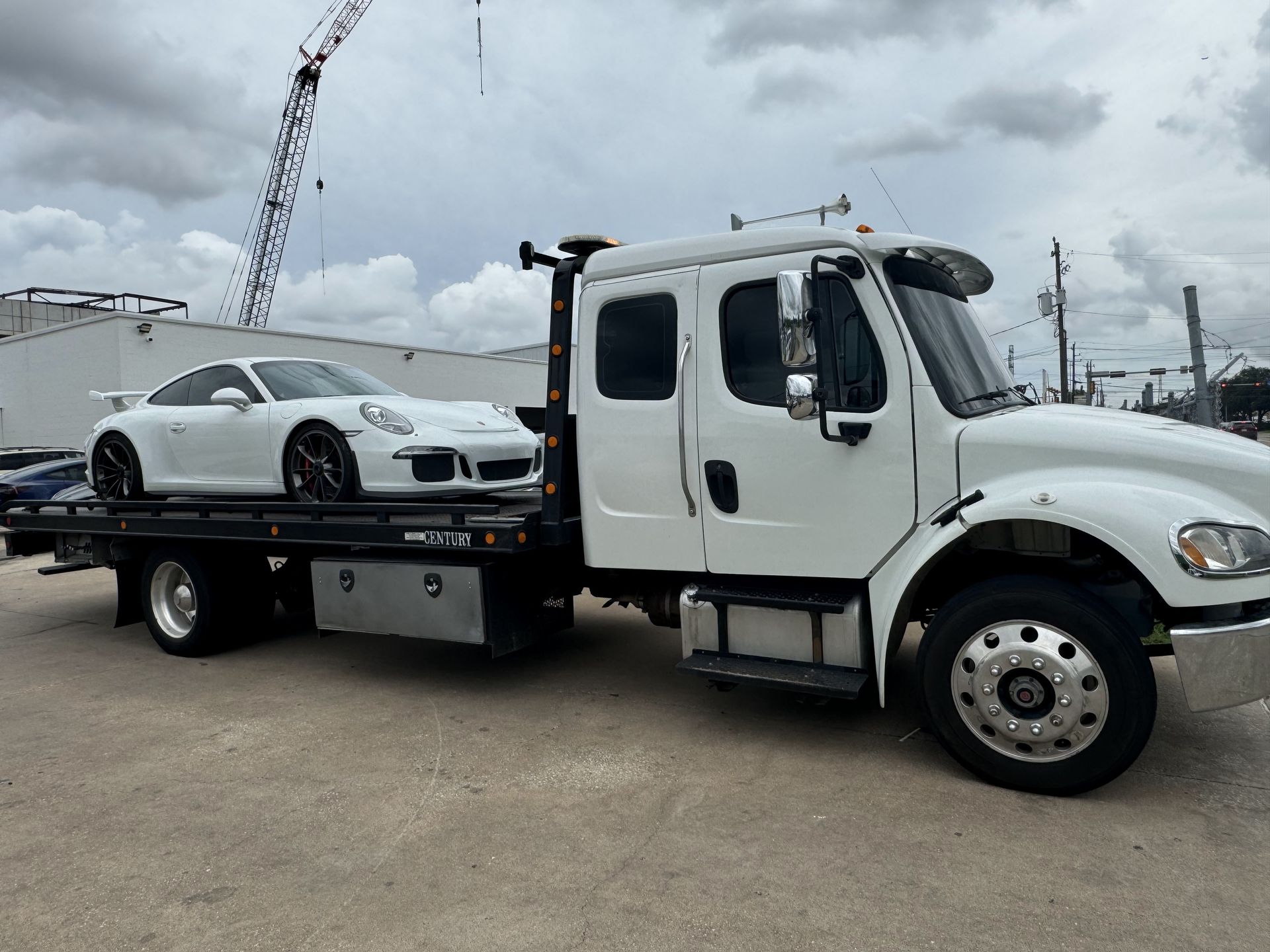White Porsche sports car loaded on a white tow truck. Outdoor setting, cloudy sky.