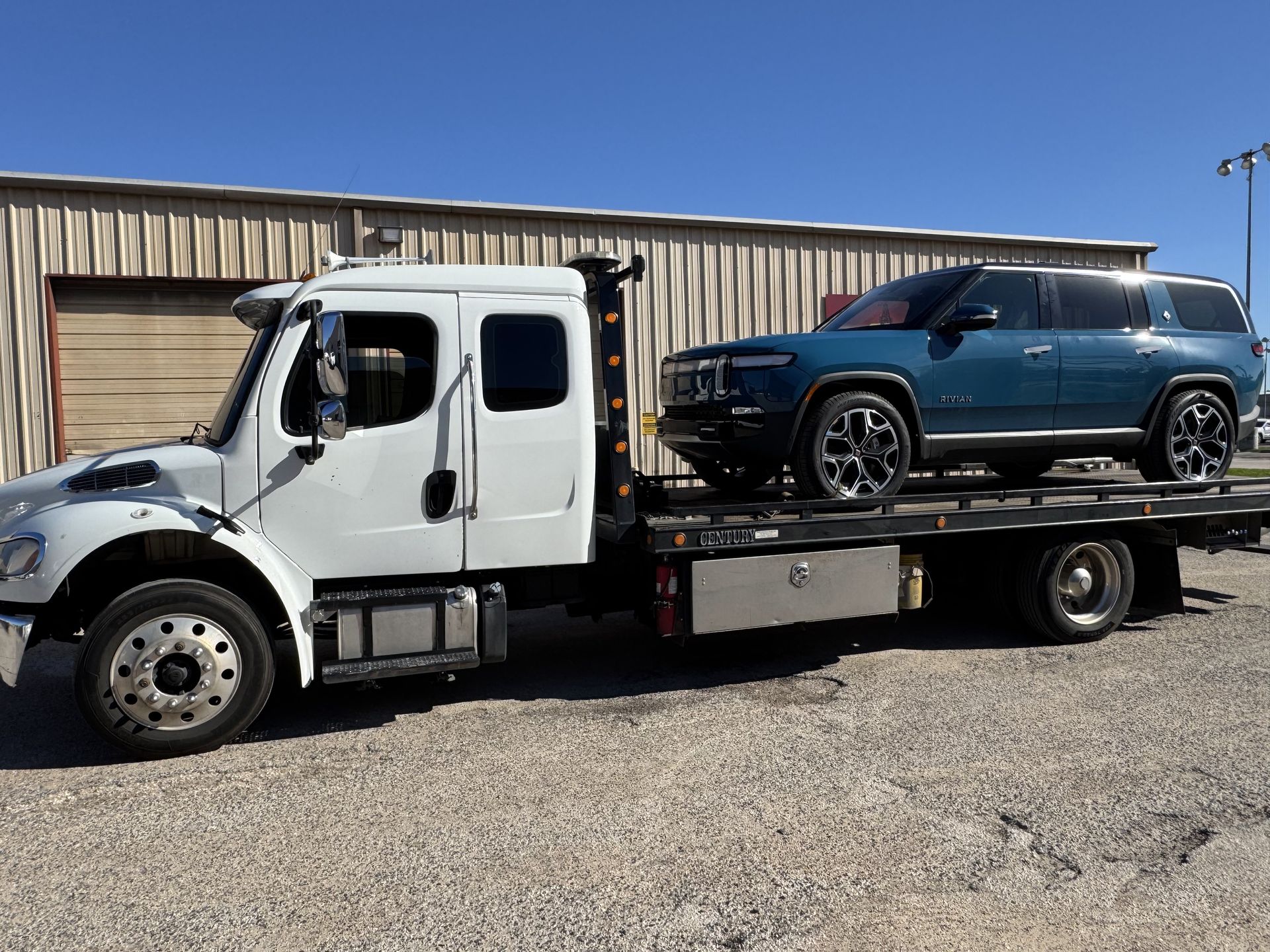 A blue Rivian SUV is being towed by a white tow truck on a sunny day.