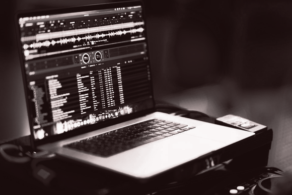 Laptop displaying a DJ software interface, in a dimly lit environment.