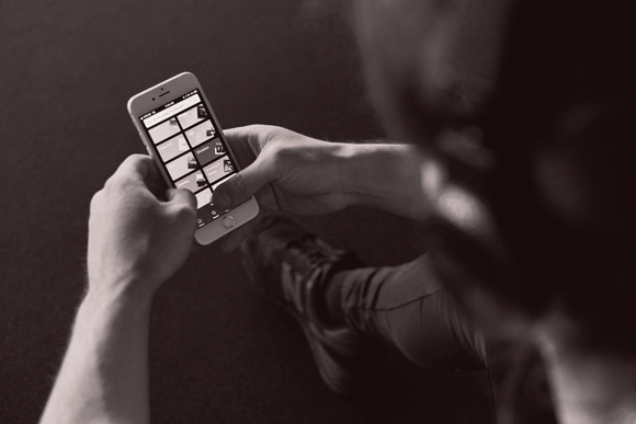 Person holding a smartphone, scrolling through a social media feed with images in sepia tone.