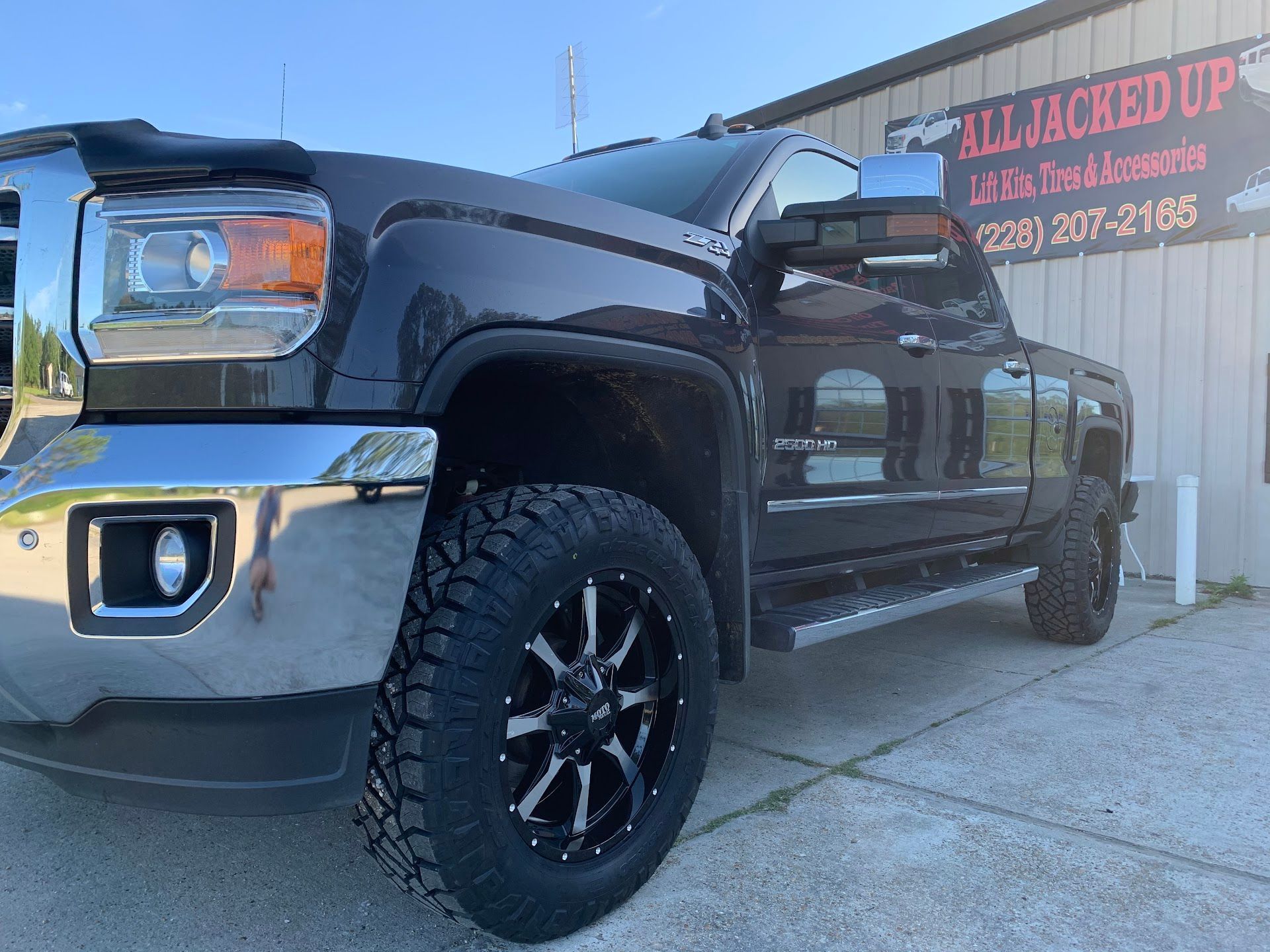 Dark pickup truck parked outside a business with black rims and off-road tires.