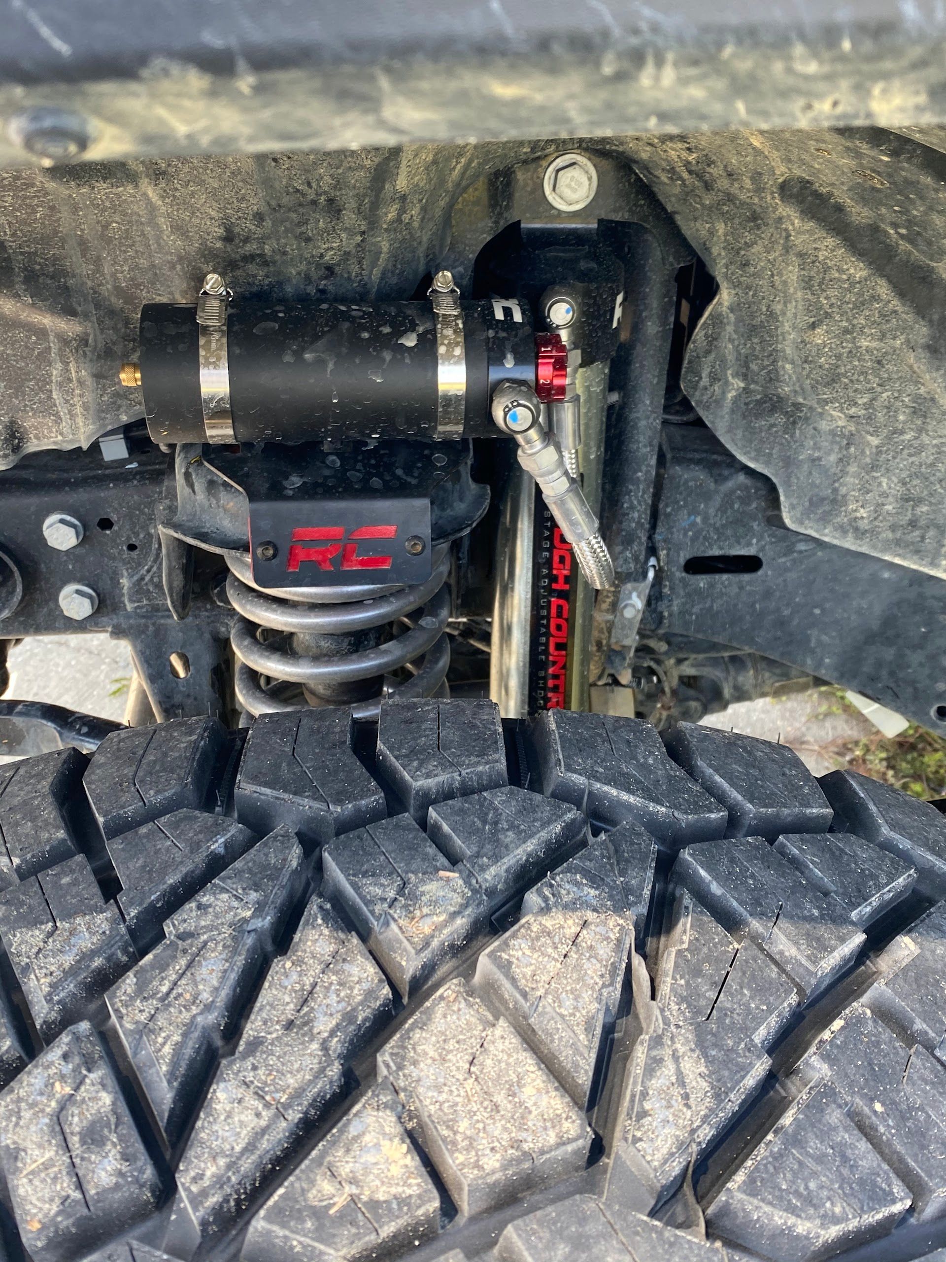 Close-up of a vehicle's suspension system, with a coil spring, shock absorber, and reservoir visible. | All Jacked Up
