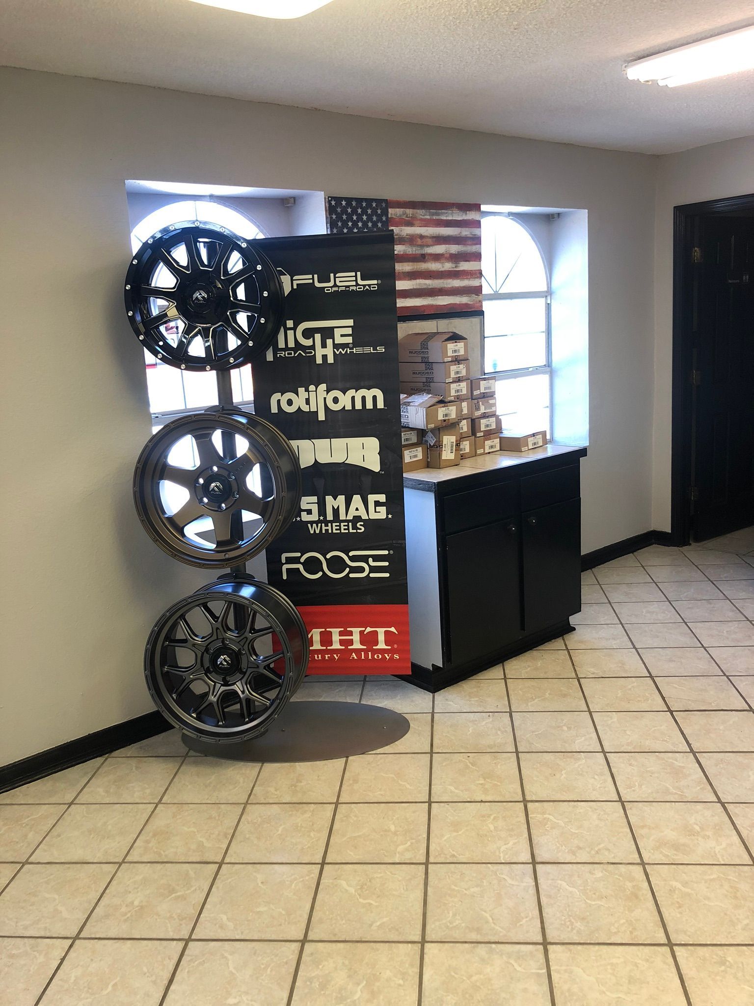 Wheels displayed in a showroom with a banner, an American flag, and a black cabinet.