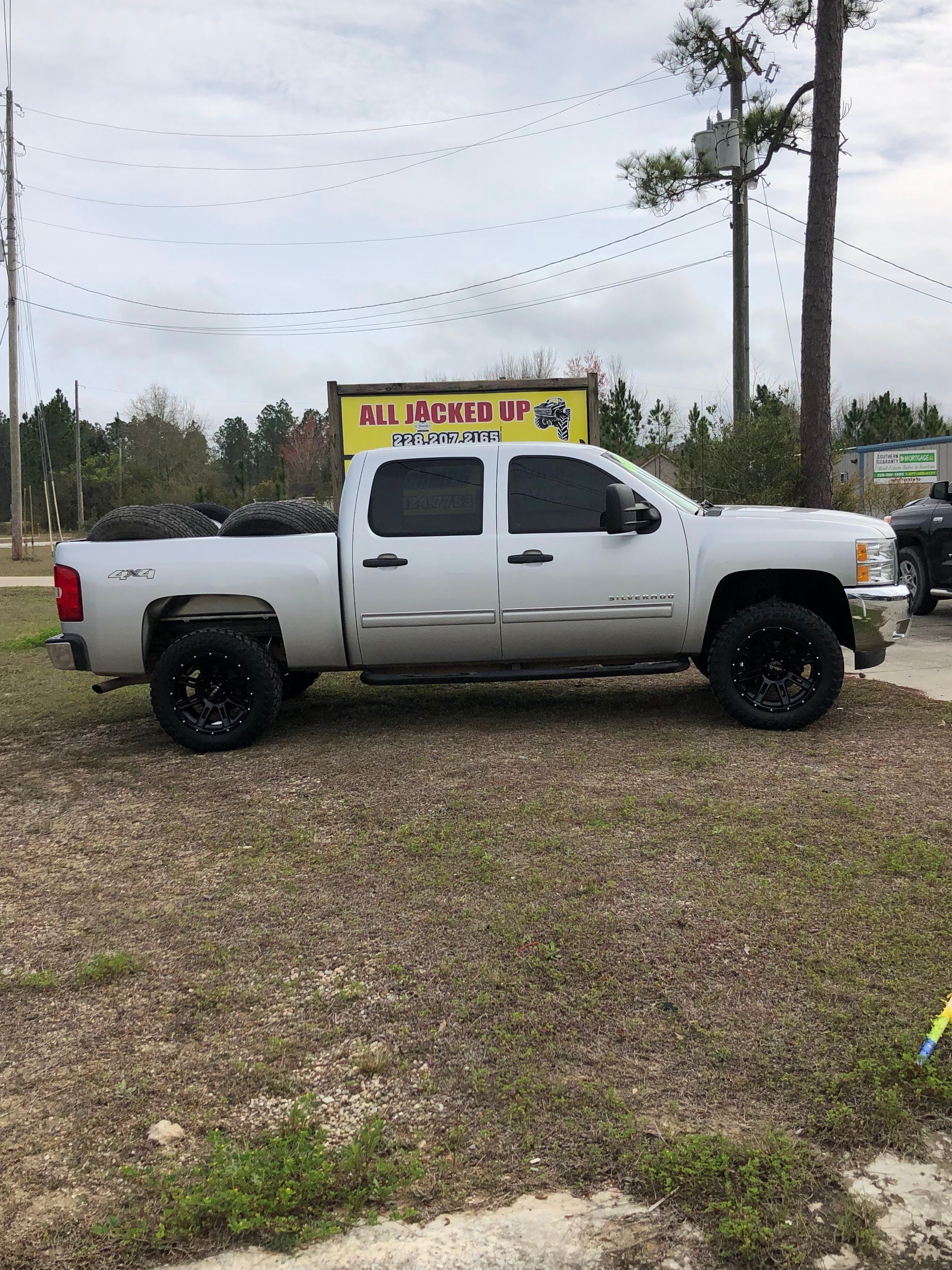 White pickup truck parked outside a business with black wheels on brown grass under a cloudy sky.