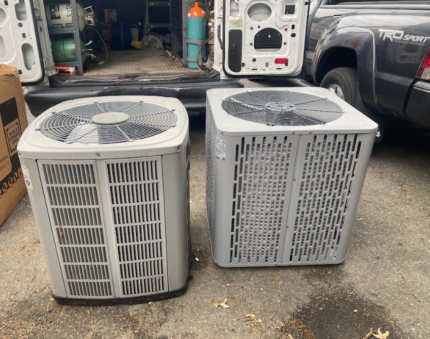 A boy is standing next to two air conditioners in front of a van.
