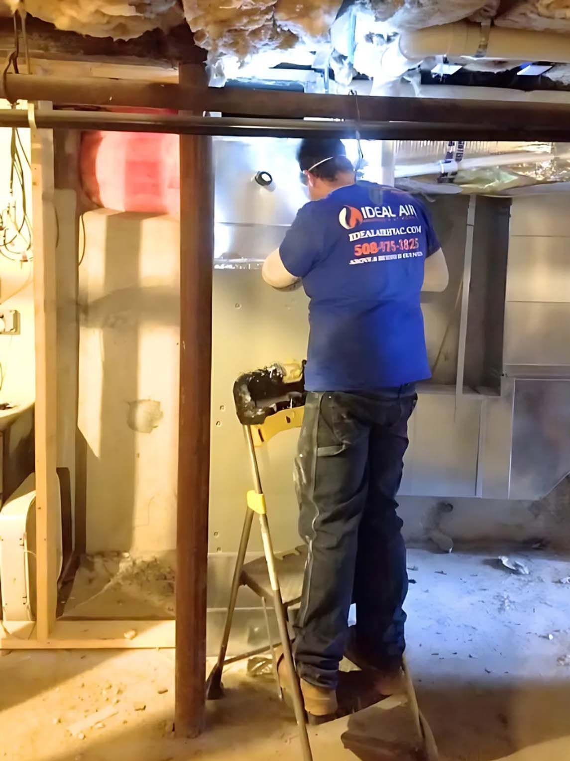 A man in a blue shirt is standing on a ladder in a basement.