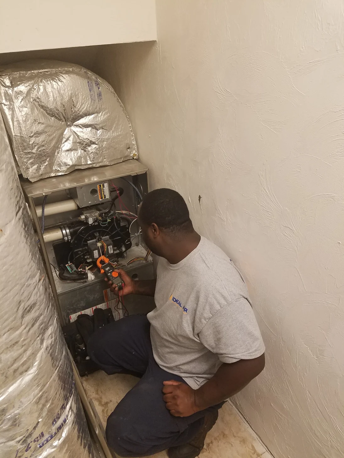 A man is kneeling down in a room working on a heater.