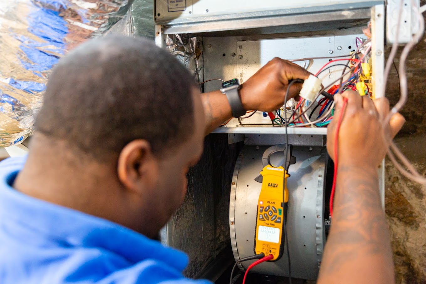 A man is working on an air conditioner with a multimeter.