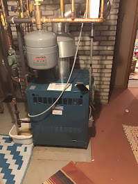 A blue boiler is sitting in a basement next to a brick wall.