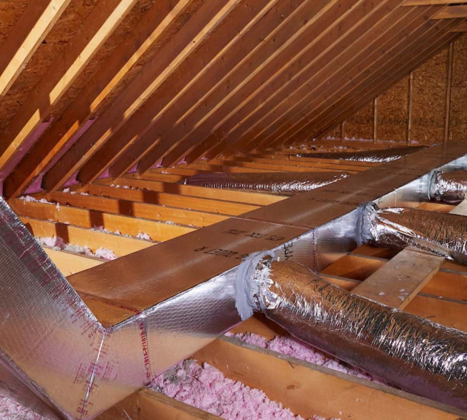 An attic with aluminum ducts and pink insulation