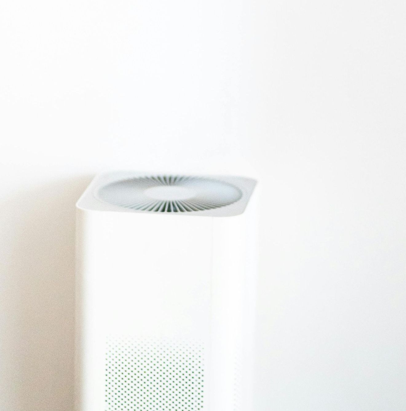 A white air purifier is sitting next to a white wall.