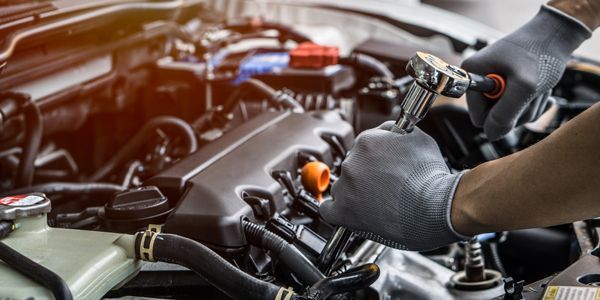 A person is working on the engine of a car with a wrench.