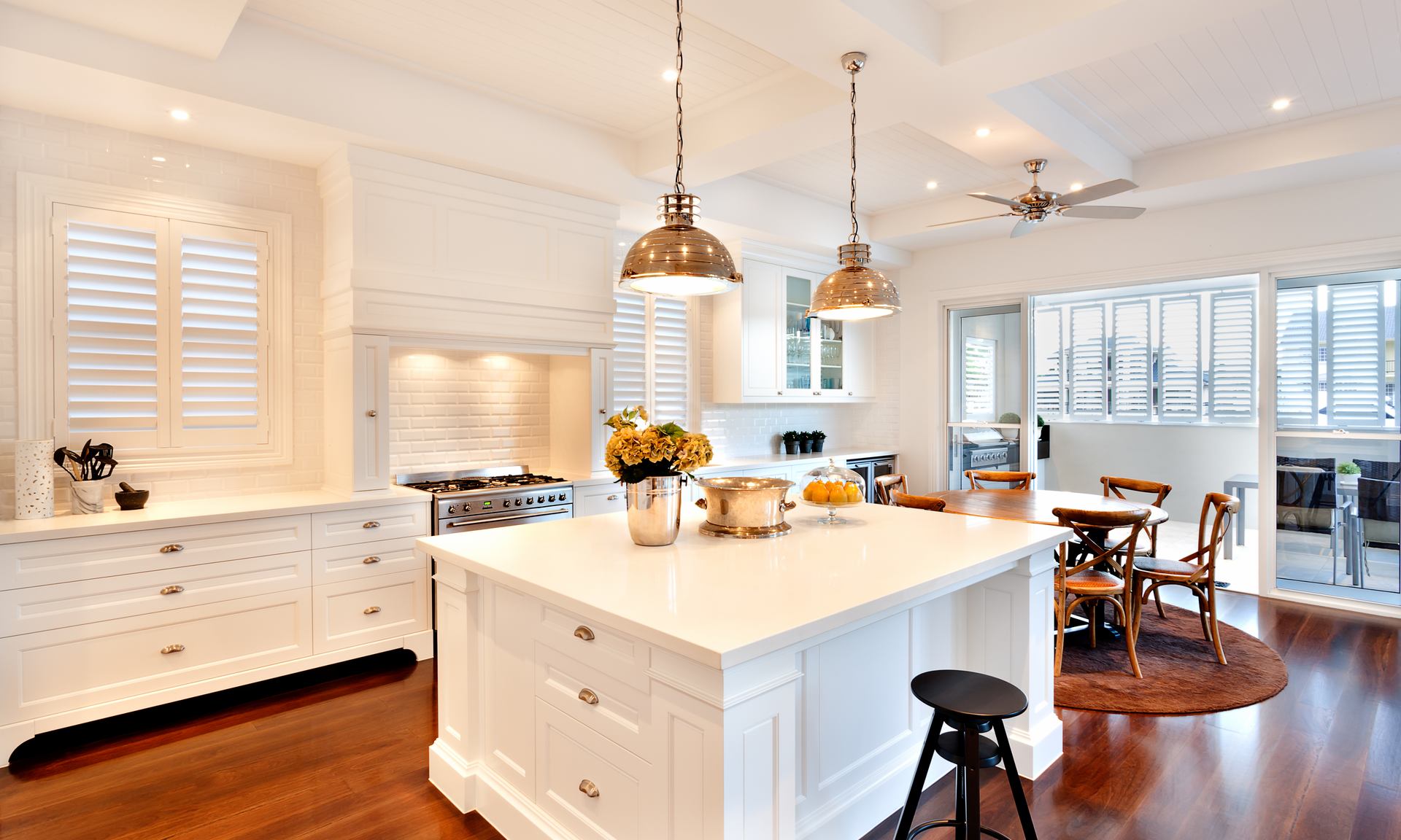 a photo of a complete kitchen with all-white cabinetry and walls. There are two low-hanging light fixtures above the island and dark red/brown hardwood flooring.