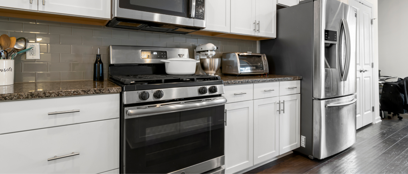 a photo of stainless steel appliances with black accents in a kitchen. There is an oven, a microwave, a refrigerator, and a toaster oven. 