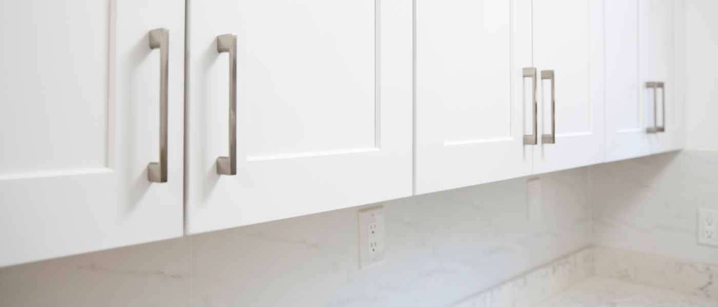 photo of white kitchen cabinets with silver handles and white kitchen walls with a gray and white tile backsplash 