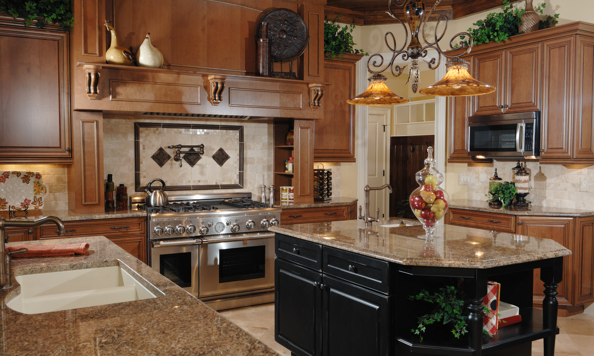 a photo of a kitchen with brown and black cabinetry and tan-colored countertops. The island cabinets are black and the kitchen cabinets are a redish brown.