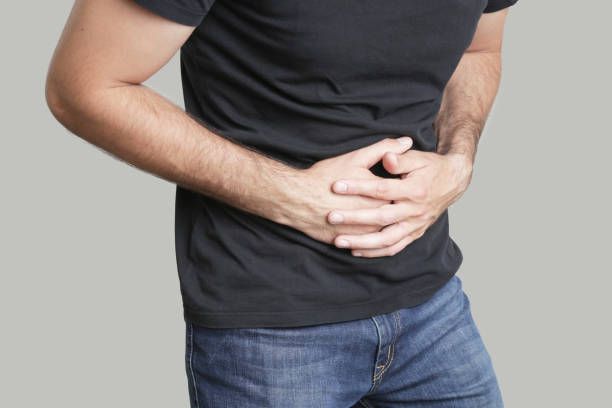 A Man In A Black Shirt Is Holding His Stomach In Pain – Dunbar, WV - Smith & Jones Chiropractic