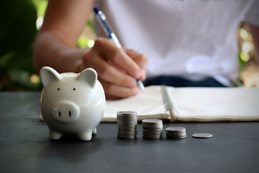 A Person Is Writing In A Notebook Next To A Piggy Bank — Christies Accountants & Advisors In Dubbo, NSW