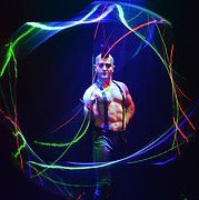 Man with mohawk and suspenders in front of swirling neon light trails in a dark setting.