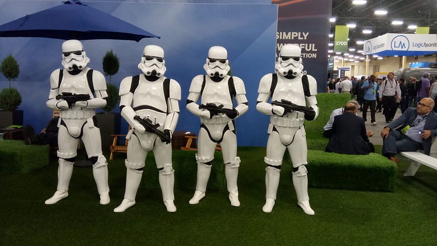 Four Stormtroopers from Star Wars posing with blasters at an event, in front of green turf and people.
