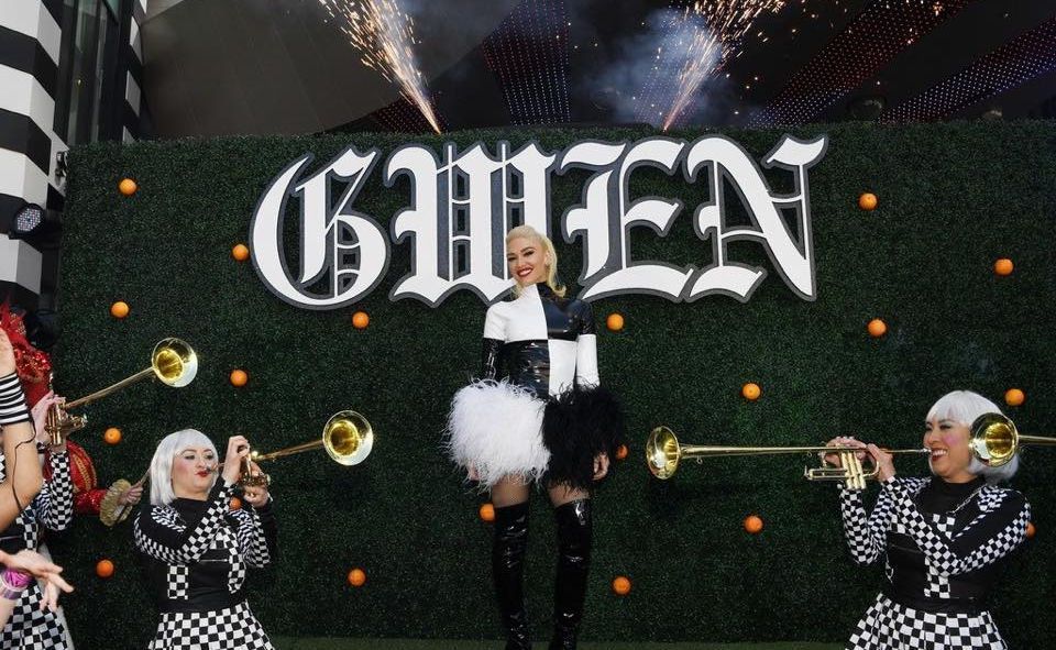 A woman is standing in front of a green hedge while playing trumpets.